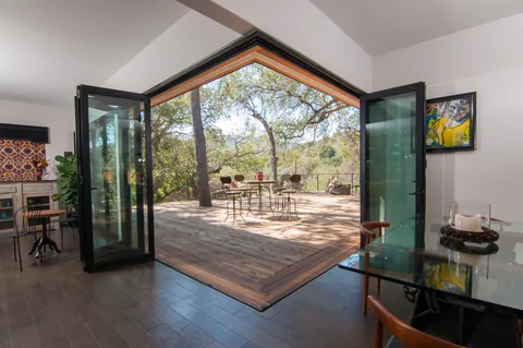 Fully open zero-post corner connecting indoor dining with a wooded deck.